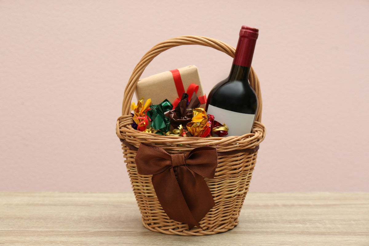 Wicker Gift Basket with Food and Wine on Wooden Table