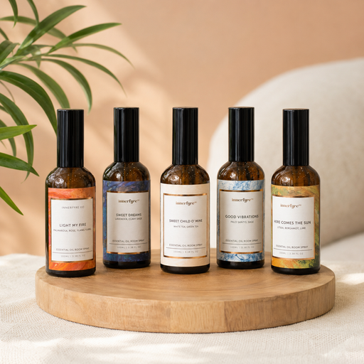 Five amber glass essential oil bottles with black caps are arranged on a round wooden tray. The bottles have different colored labels in orange, blue, cream, light blue, and green, with the brand name 'smokeyeyes' visible on each.
